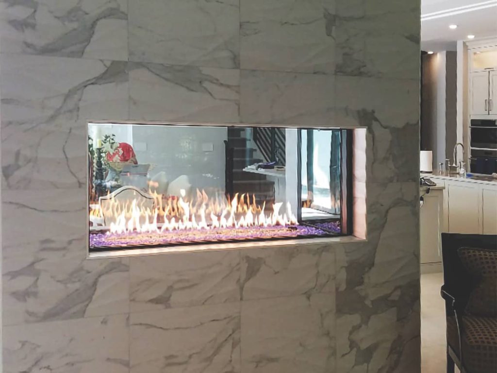 Heat & Glo Foundation See-Through custom gas fireplace with mirrored flames and crystal glass media in modern marble wall.