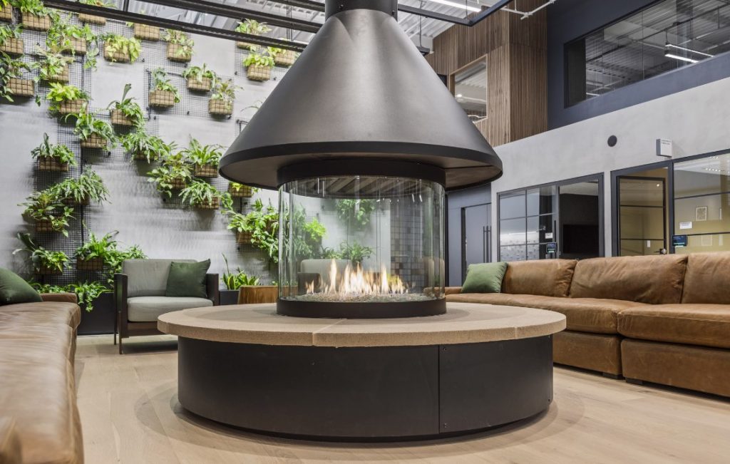 Stellar round custom fireplace in lobby with green plant wall in background