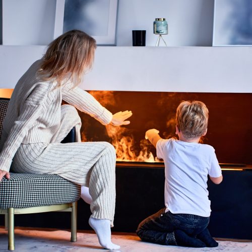 Woman,Sits,Near,Fireplace,With,Little,Boy,In,Living,Room.